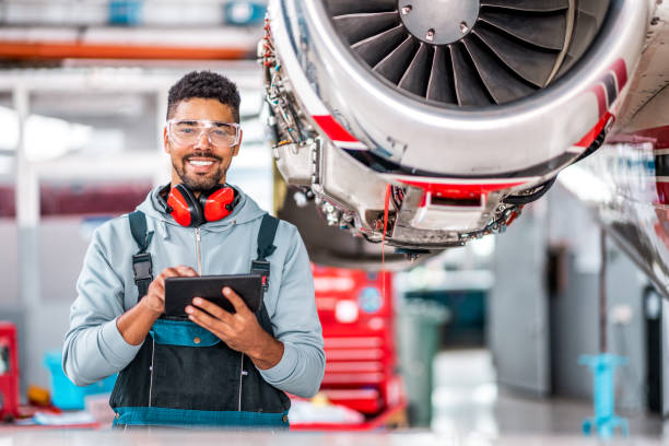 Monday Jet Aircraft Maintenance Mechanic holding a tablet in front of the Airplane Jet Engine in the Hangar